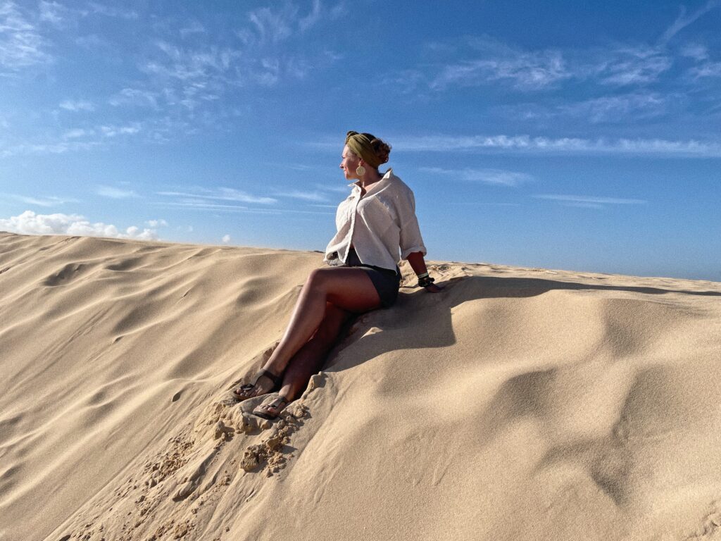 Ida sitzt auf einer Sanddüne und schaut Zichtung Sonne